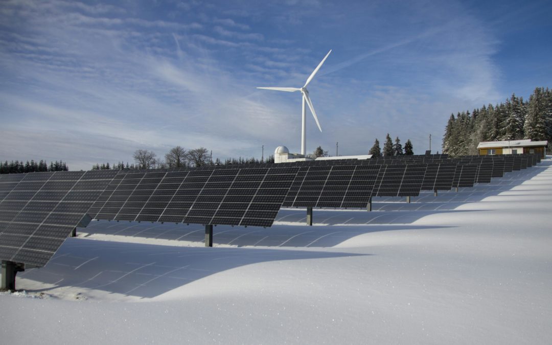 Panneaux solaires en premier plan avec un éolienne en arrière-plan.