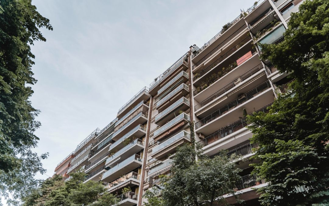 Un grand immeuble résidentiel moderne avec de nombreux balcons, vu d'en bas, encadré par des arbres.